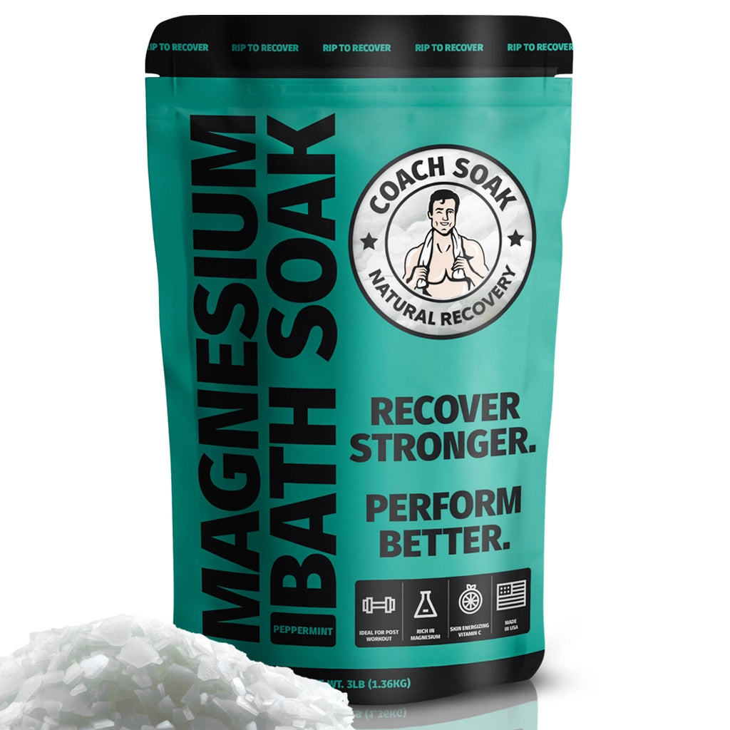 A package of Coach Soak: Muscle Recovery Bath Soak with the tagline "recover stronger. perform better." featuring coaching iconography and a peppermint scent, positioned next to a pile of white bath salts.