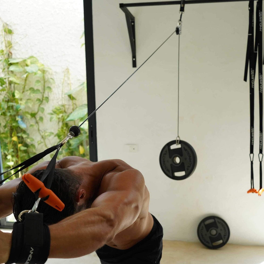 A person engaged in a concentrated cable pulley workout, focusing on their upper-body strength with A90 Ankle Straps in a home gym setting.