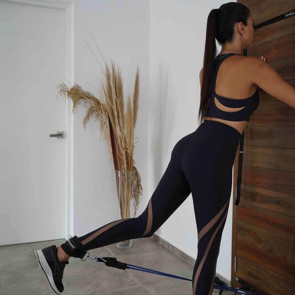 A woman in athletic wear performing a leg curl substitution exercise with A90 Ankle Straps and a resistance band attached to a door.
