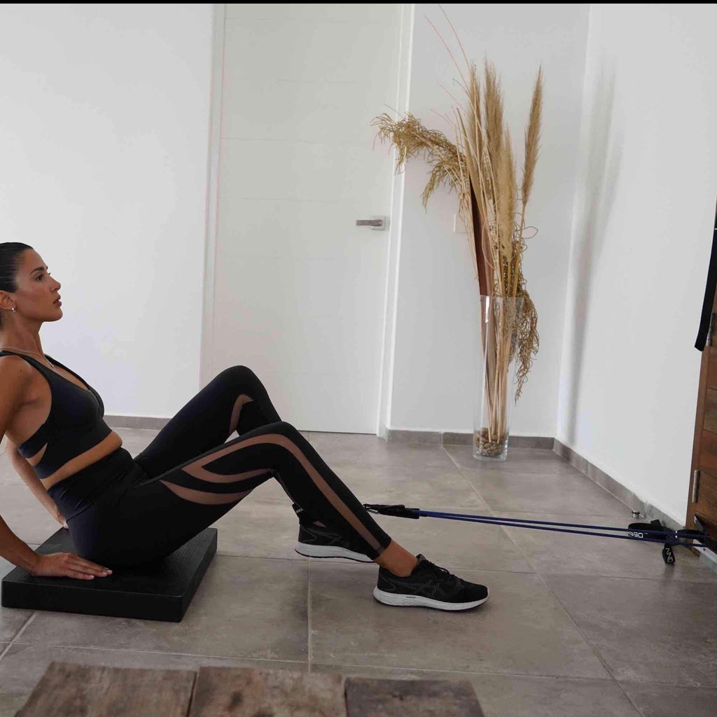 A focused individual performing a leg day resistance band workout with A90 Ankle Straps in a minimalist, modern space.