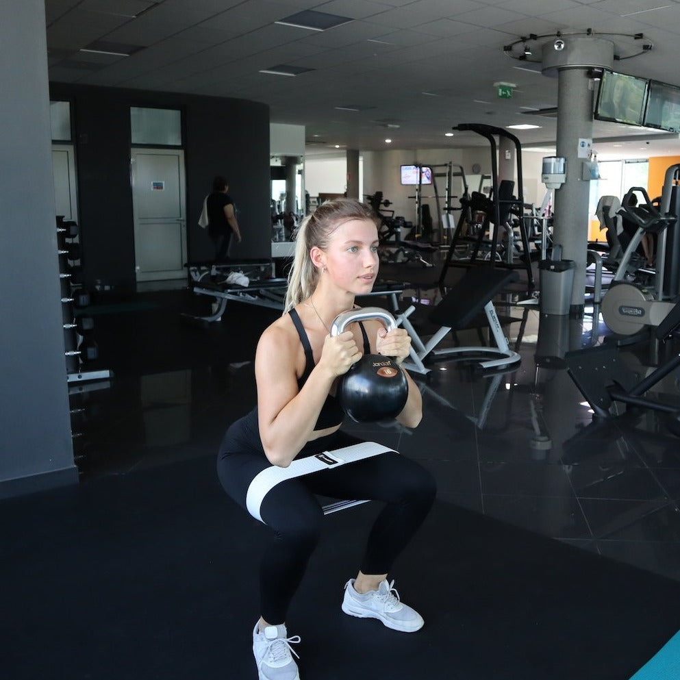 Focused woman performing a goblet squat with A90 Hip Bands at the gym.