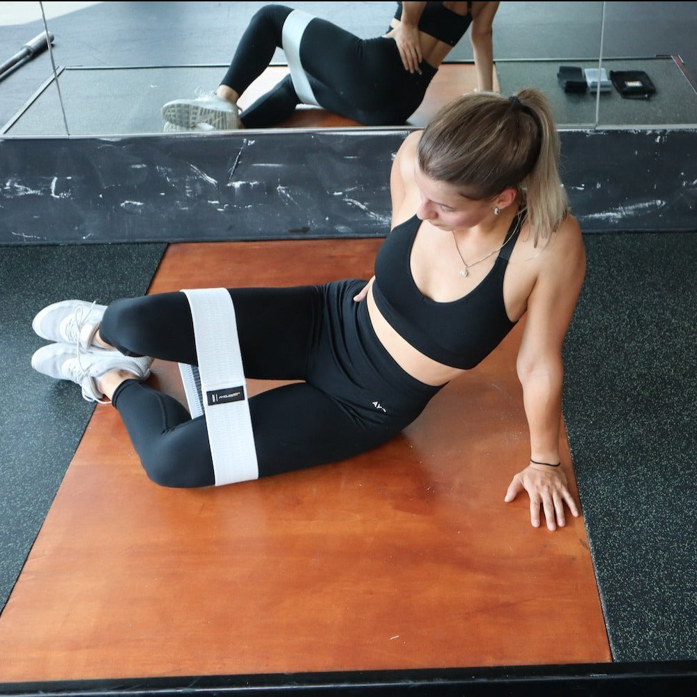 A focused woman exercises with the A90 Leg Day Set around her thighs, performing a seated workout on a gym mat.